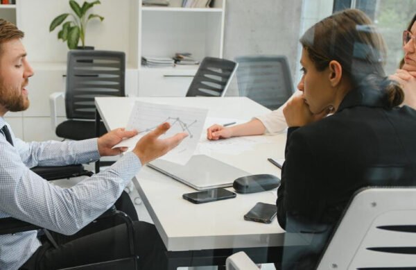 Inclusão: 2 mulheres e 1 homem em cadeira de rodas conversam em uma sala de reunião.