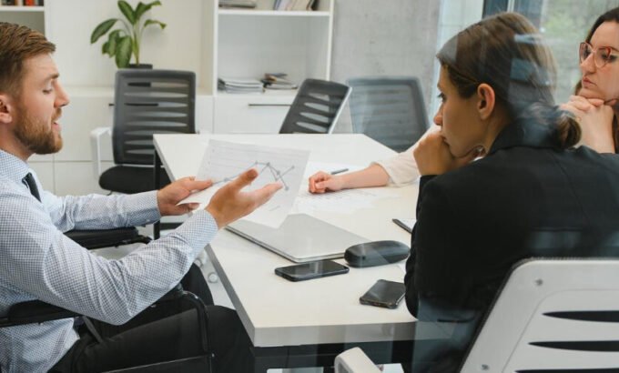 Inclusão: 2 mulheres e 1 homem em cadeira de rodas conversam em uma sala de reunião.