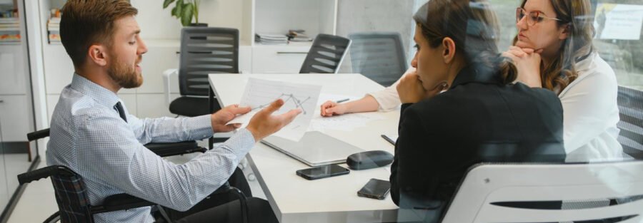 Inclusão: 2 mulheres e 1 homem em cadeira de rodas conversam em uma sala de reunião.